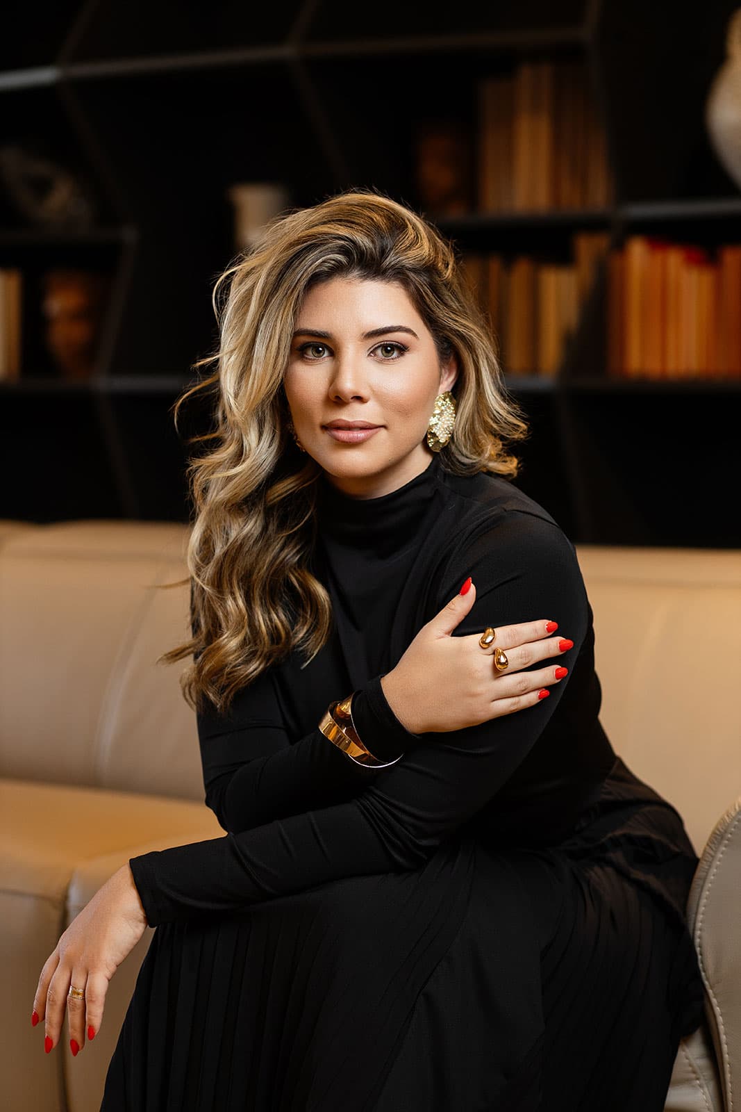 Bia Munareto sentada, vestido preto, em uma biblioteca